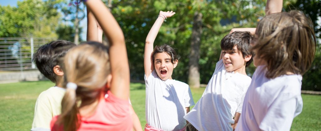 Group of children playing with raised arms in a sunny park, enjoying summer fun.